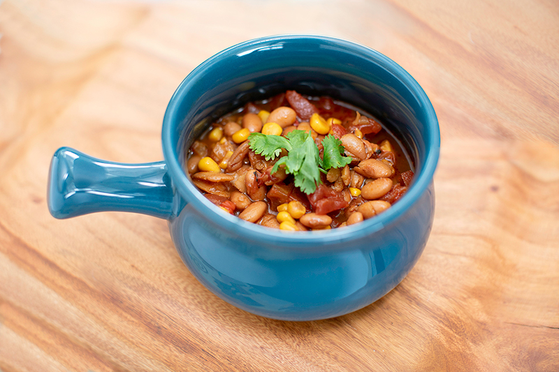 pinto bean soup with a green garnish in a blue soup bowl on a light wood surface.
